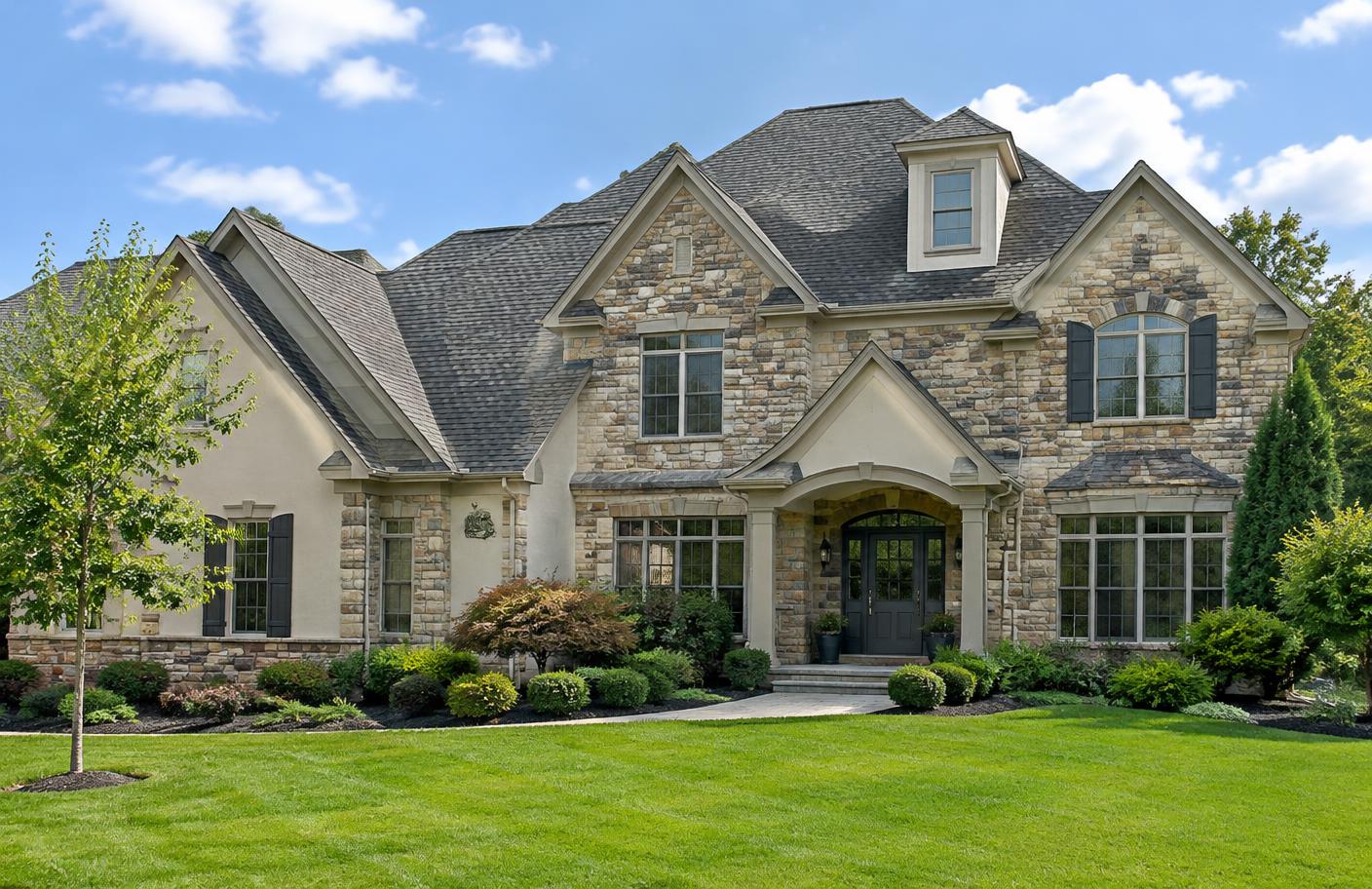Stone home with a complex shingle roof, dormers, and valleys